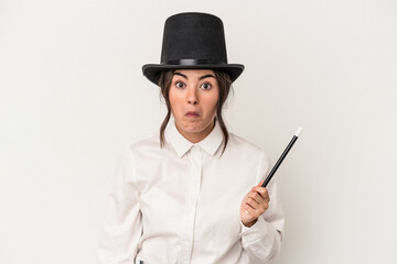 Young magician woman holding a wand isolated on white background shrugs shoulders and open eyes confused.