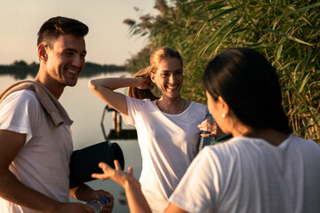 Group of people talking after yoga exercises by the lake at sunset.