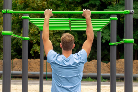 Young man exercising on horizontal bar outdoors. Back view