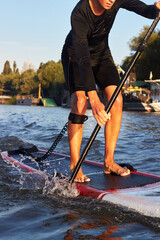 Cropped image of handsome young man stand up paddle surfing on the river