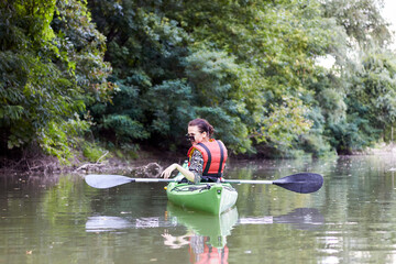 Fototapeta na wymiar Young woman sits in kayak at river near green trees