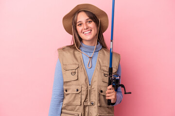 Young caucasian fisherwoman holding a rod isolated on pink background happy, smiling and cheerful.