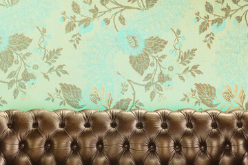 Old chesterfield sofa in front of wallpaper with a floral pattern