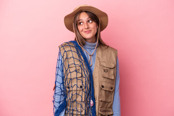 Young caucasian fisherwoman holding a net isolated on pink background dreaming of achieving goals and purposes