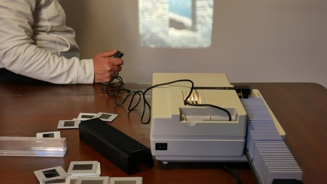 antique white slide projector seen from the side, from above with the slides scattered, the light of the proiector projected on the white wall, 