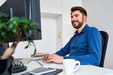 Cheerful man working at home using laptop with external monitor