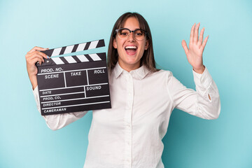 Young caucasian woman holding clapperboard isolated on blue background receiving a pleasant...