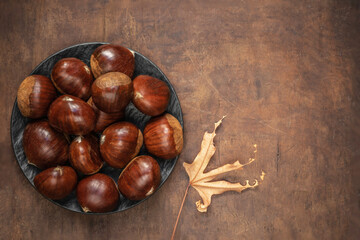 Obraz premium Sweet chestnuts on old rustic wooden table with plenty of copy space. Autumn fall concept. Horse chestnuts top view.