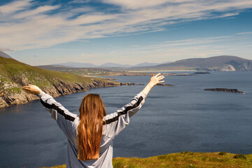 Red hair teenager girl with her hands up in the air with excitement. Magnificent view of Keem bay...