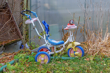 An old children's scooter is parked near a plastic fence next to unnecessary things on an autumn day