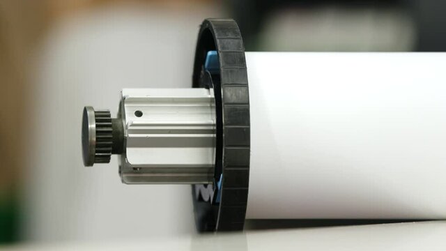 A staff member slides a roll holder into a large white paper roll.