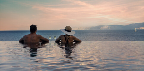 couple enjoying romantic view to the sea and drinking champagne in infinity pool at luxury resort....