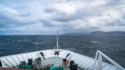 Schiff im Sturm, in Nordnorwegen k&auml;mpft sich ein Linienschiff durch die Wellen, Schaumkronen tanzen auf den Wellen. st&uuml;rmischer Atlantik unter dunklen Wolken. rollende See auf der Reise in Norwegen.