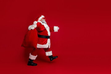 Photo of pretty cool santa claus wear red costume dark eyewear walking holding gifts sack empty space isolated red color background