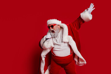 Photo of funny carefree entertainer retired man hold mic sing wear santa hat costume isolated red...