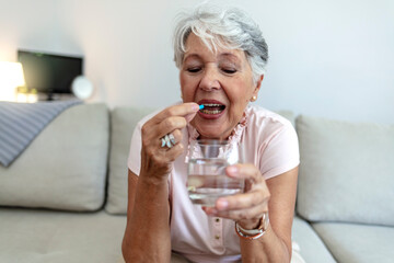 Shot of a senior woman about to take a pill. Woman holding pill and glass of fresh water, taking medicine from headache, stomach pain or taking vitamins, sedation meds. Healthcare and people concept.