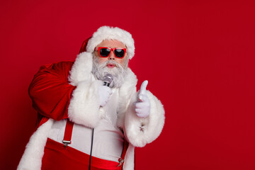 Photo of cool funny santa claus wear red costume dark eyewear singing karaoke pointing finger you empty space isolated red color background