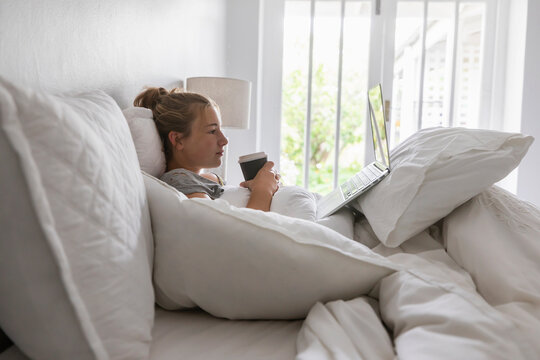 teenage girl lying in bed using laptop