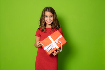 Smiling Young girl in red dress holding gift box and looking at the camera over green background