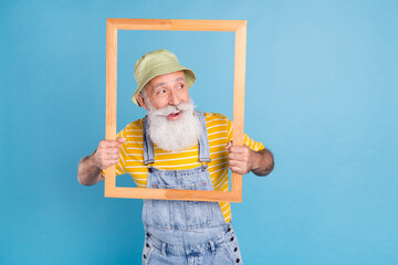 Photo of aged man happy positive smile curious interested look empty space wooden frame isolated over blue color background