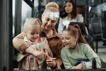 Portrait of adult woman with two kids having fun on bus while traveling by public transport in city