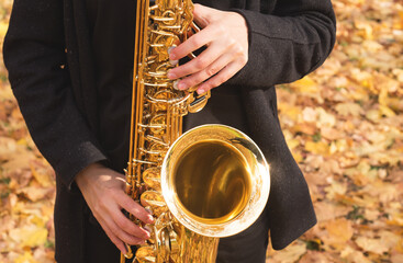 Fototapeta premium The girl musician plays the saxophone. Close-up of a golden saxophone on a background of yellow leaves.