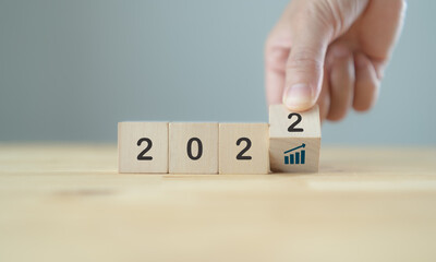 Business growth concept in 2022  for business plan and strategy. Hand flips wooden cubes "2022" and performance growth symbol on  grey background, copy space. Banner for new action plan ,annual plan.