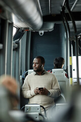 Vertical portrait of African-American man looking at window in bus while traveling by public...