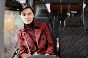 Portrait of elegant mature woman sleeping on bus while traveling by public transport in city, copy...