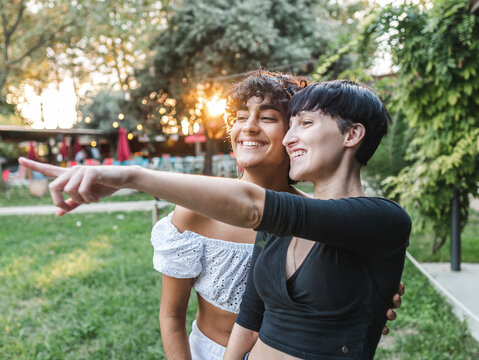 Cheerful multiracial couple of women pointing away