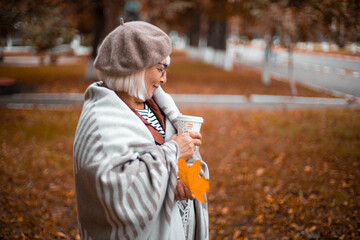 Lady in a warm wool blanket holds a paper cup of hot chocolate or coffee drink while enjoying the...