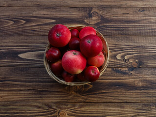 Wicker basket with red ripe apples on rustic wooden table background. Close up of object, top view. Bowl, container with fresh fruits, raw ingredient, natural food. Fall, autumn harvest, thanksgiving