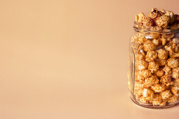 glass jar with sweet caramel popcorn with place for text on beige background