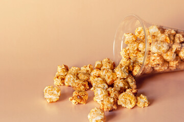 sweet caramel popcorn sprinkled from a plastic cup with a place for text on a beige background