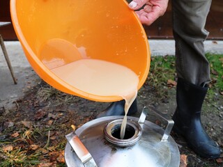 a farmer making homemade wine from apples, pouring apple mash into the tank of an alcohol apparatus...