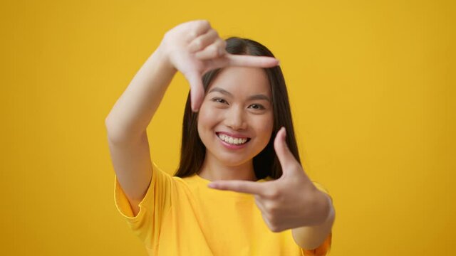 Asian Woman Looking Through Finger Frame Taking Photo, Yellow Background