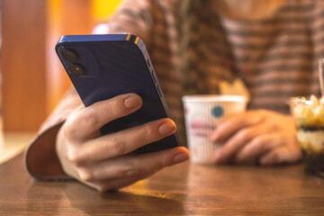 Young lady using mobile phone in cafe with coffe cup in hands on a wooden table. Public places concept photo