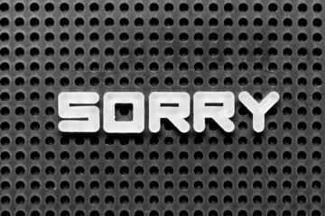 White alphabet letter in word sorry on black pegboard background