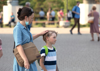 mother is walking with her little son in street in sunny summer day and stroke him on hair