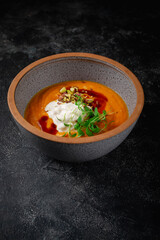 Pumpkin cream soup mashed with spices and a sprig of peas on a dark stone table