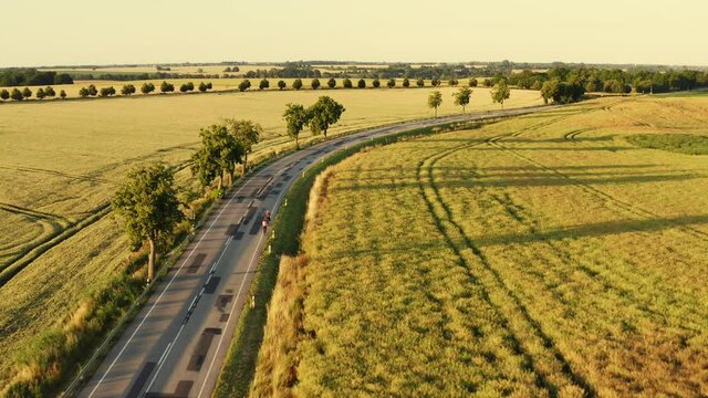 Drone flight along a country road. There are 2 cyclists on the road. The drone follows them around a bend. Aerial View of 2 Bikers.
