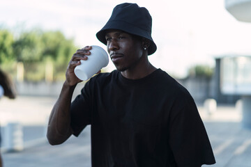 Chico negro atlético vestido completamente de negro sobre fondo claro con vaso de cafe