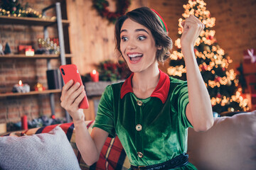 Photo of young shocked amazed positive santa helper woman hold phone winner indoors inside house...