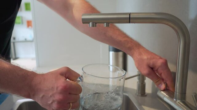 Man open faucet tap and fill jug with clear water at bright kitchen. Closeup