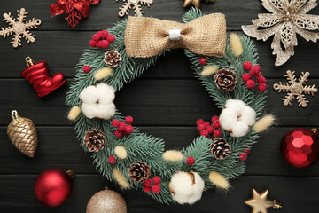 Wreath from fir, pine and spruce twigs, decorated with cotton, flowers ad christmas decoration on black wooden background