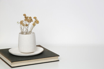 Ceramic mug with dry Everlasting flowers on books with on the table. Simple home decor.