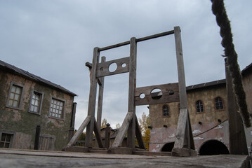 Scaffold with two blocks for criminals against the background of houses of an abandoned medieval city. Medieval execution weapon - obrazy, fototapety, plakaty