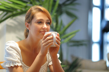 Happy woman drinking coffee at home looking away