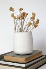 Ceramic mug with dry Everlasting flowers on books with on the table. Simple home decor.