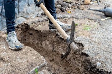 A man picks up hard ground with a pickaxe while digging a ditch on a construction site